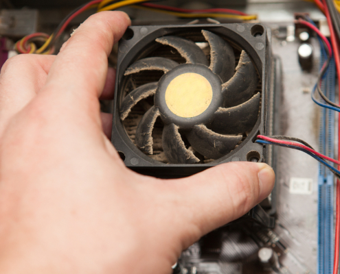 Eine Hand, die einen staubigen Computerlüfter in einem Computergehäuse hält, mit sichtbaren Kabeln und Komponenten im Hintergrund - perfekt für den Säubere-deinen-Computer-Tag und eine Erinnerung daran, den Computer regelmäßig zu reinigen.