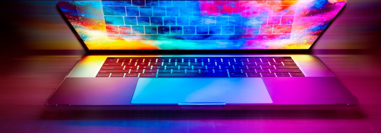 Ein Laptop, möglicherweise ein alter Computer, verfügt über einen hell beleuchteten Bildschirm, der leuchtendes rosa, blaues und gelbes Licht ausstrahlt und bunte Reflexe auf die Tastatur wirft - eine stilvolle Art, ältere Geräte in einer dunklen Umgebung sinnvoll weiterzunutzen.