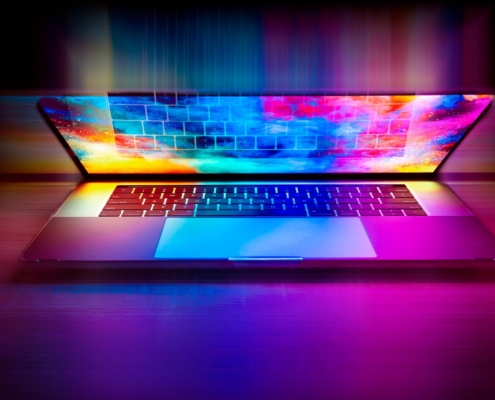 Ein Laptop, möglicherweise ein alter Computer, verfügt über einen hell beleuchteten Bildschirm, der leuchtendes rosa, blaues und gelbes Licht ausstrahlt und bunte Reflexe auf die Tastatur wirft - eine stilvolle Art, ältere Geräte in einer dunklen Umgebung sinnvoll weiterzunutzen.