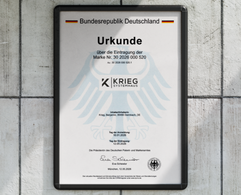 Eine gerahmte deutsche Urkunde mit dem Titel „Urkunde“, die ein schwarzes Adlerwappen und das Logo von KRIEG SYSTEMHAUS trägt und an einer hellen Wand hängt.